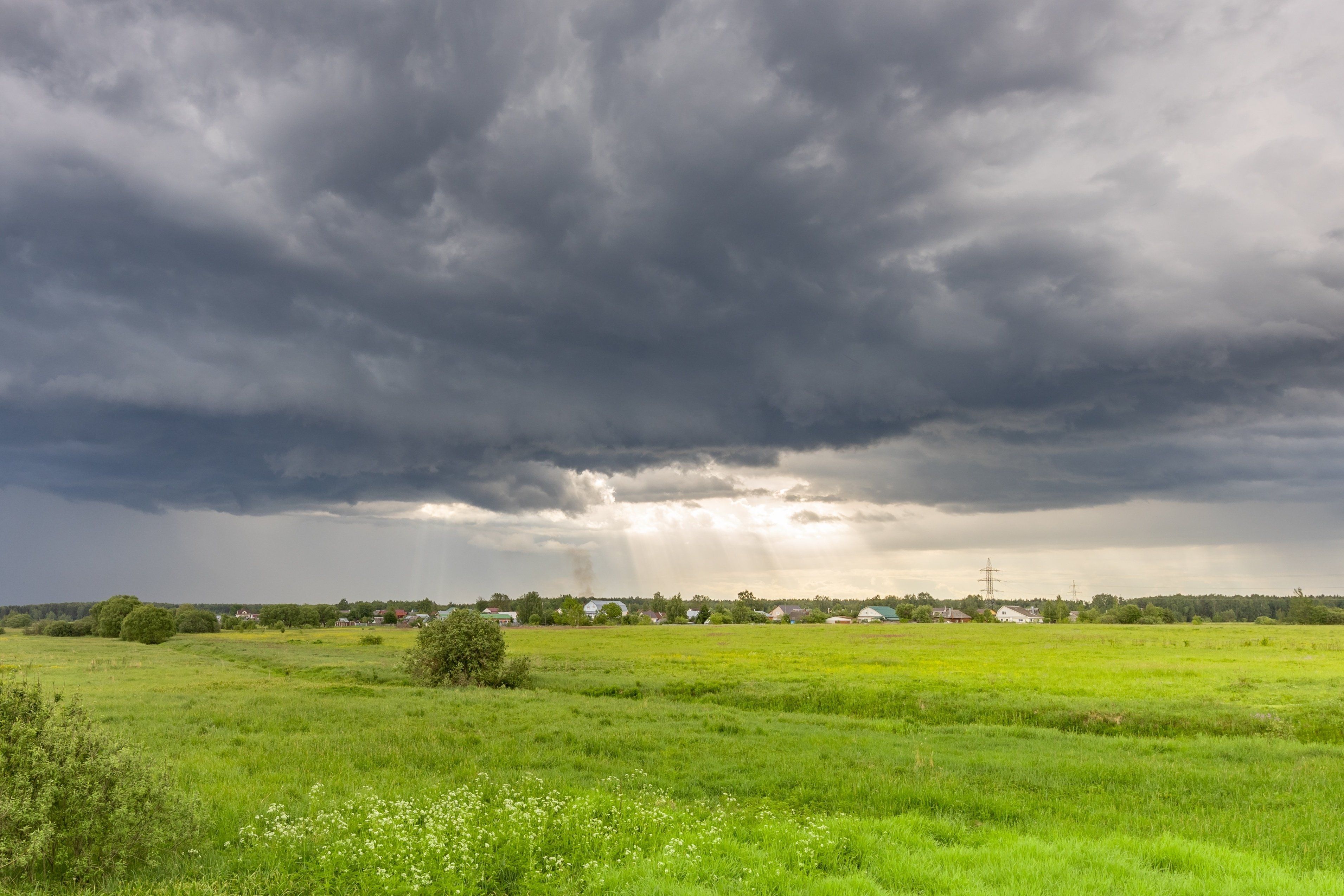 Dark,Clouds,Loom,Over,A,Vibrant,Green,Field.,Sunlight,Breaks