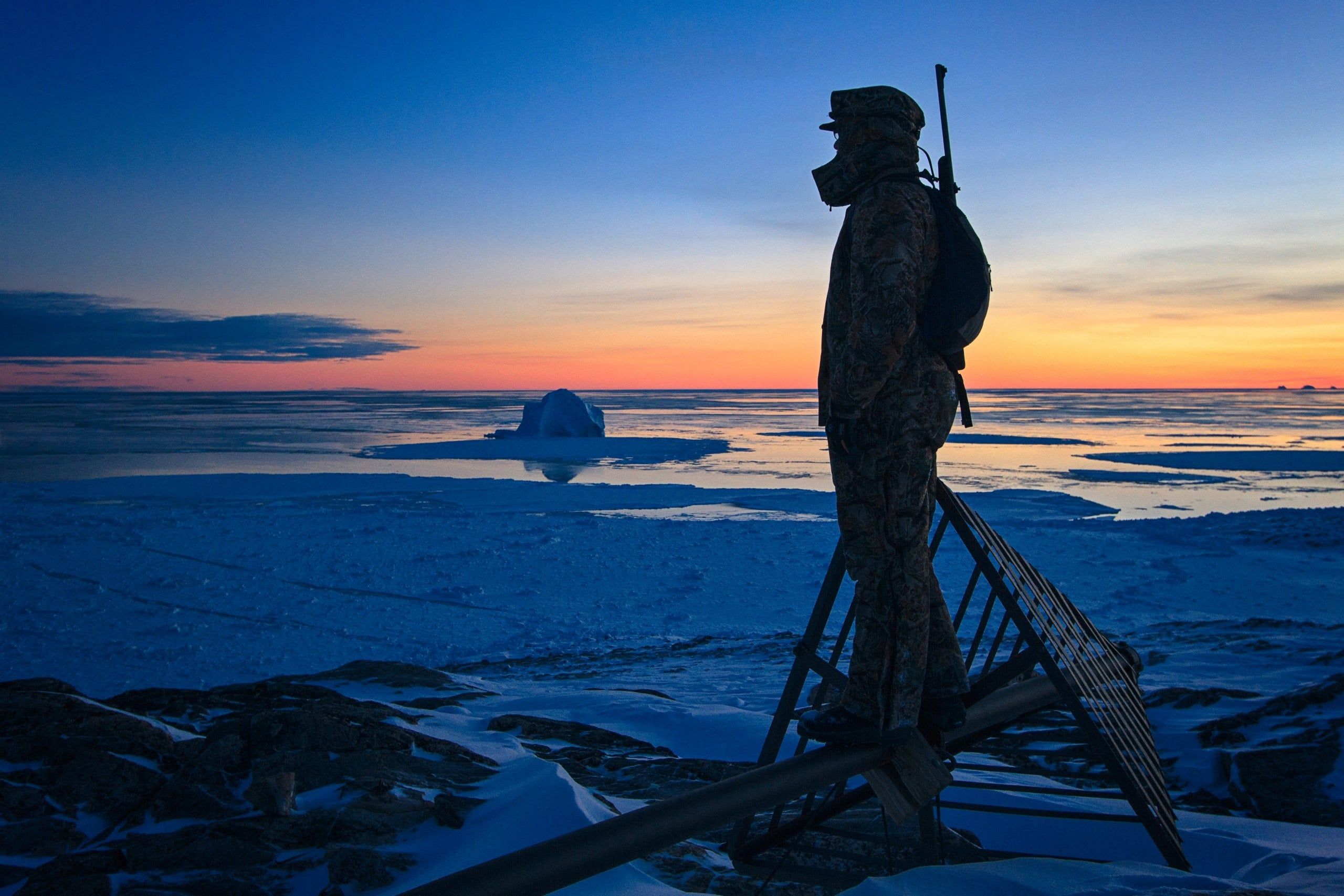 Man with rifle watches arctic sunset