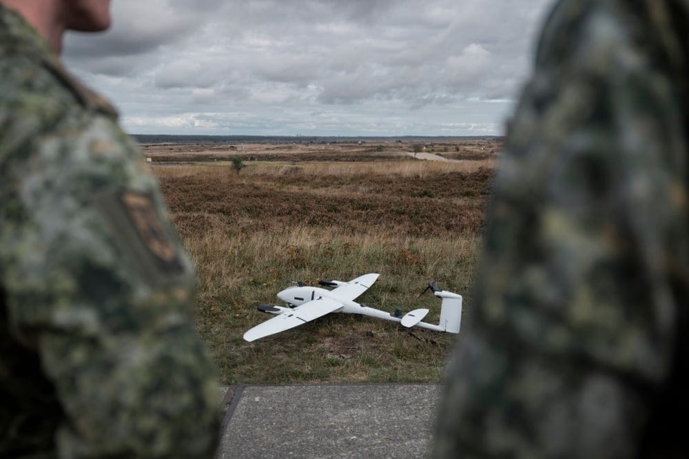 Military,Drone,On,Terrain,With,Soldiers,Observing,From,Background,During