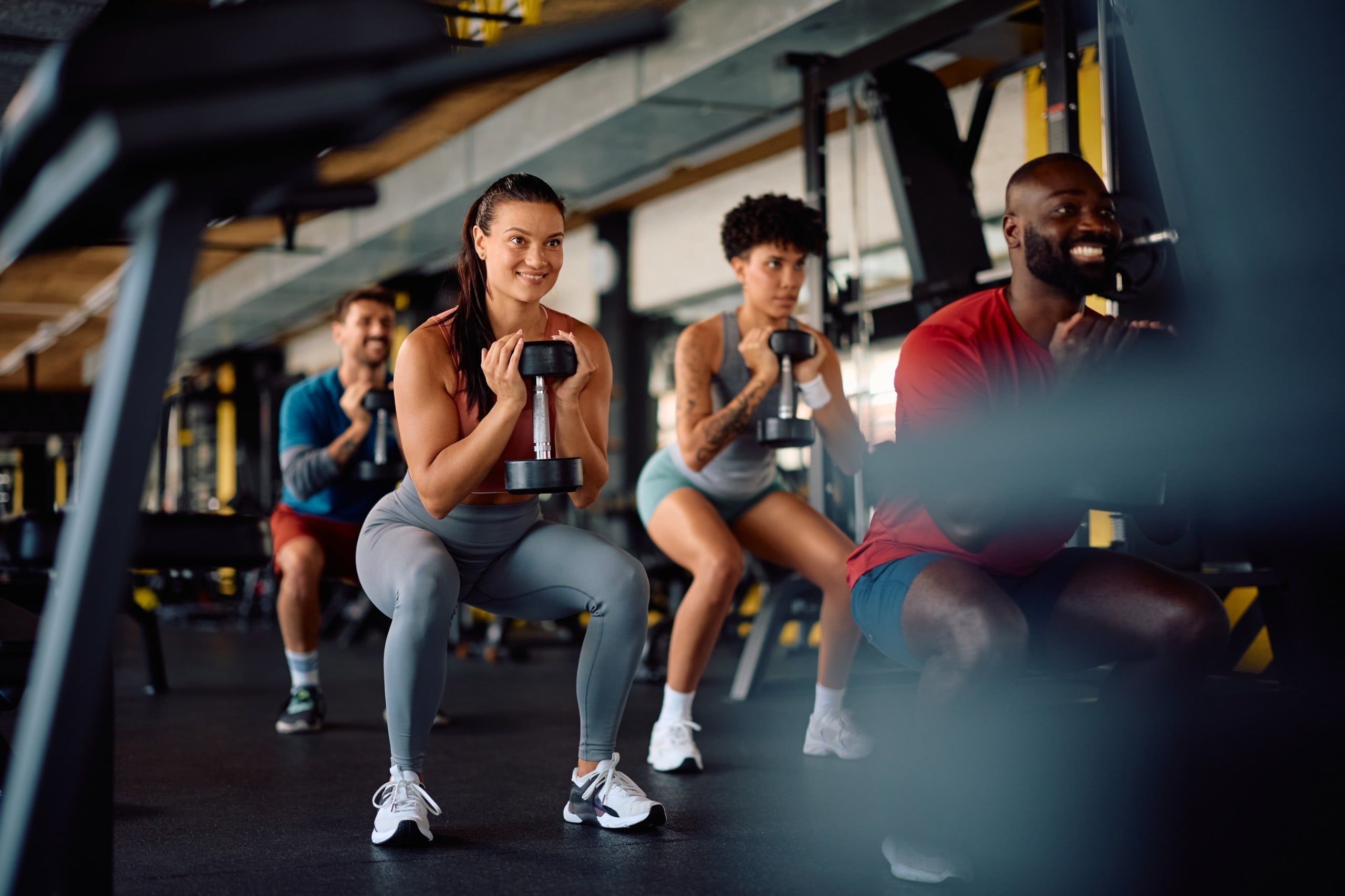 Happy,Multiracial,Athletes,In,Squatting,Position,Exercising,With,Dumbbells,In