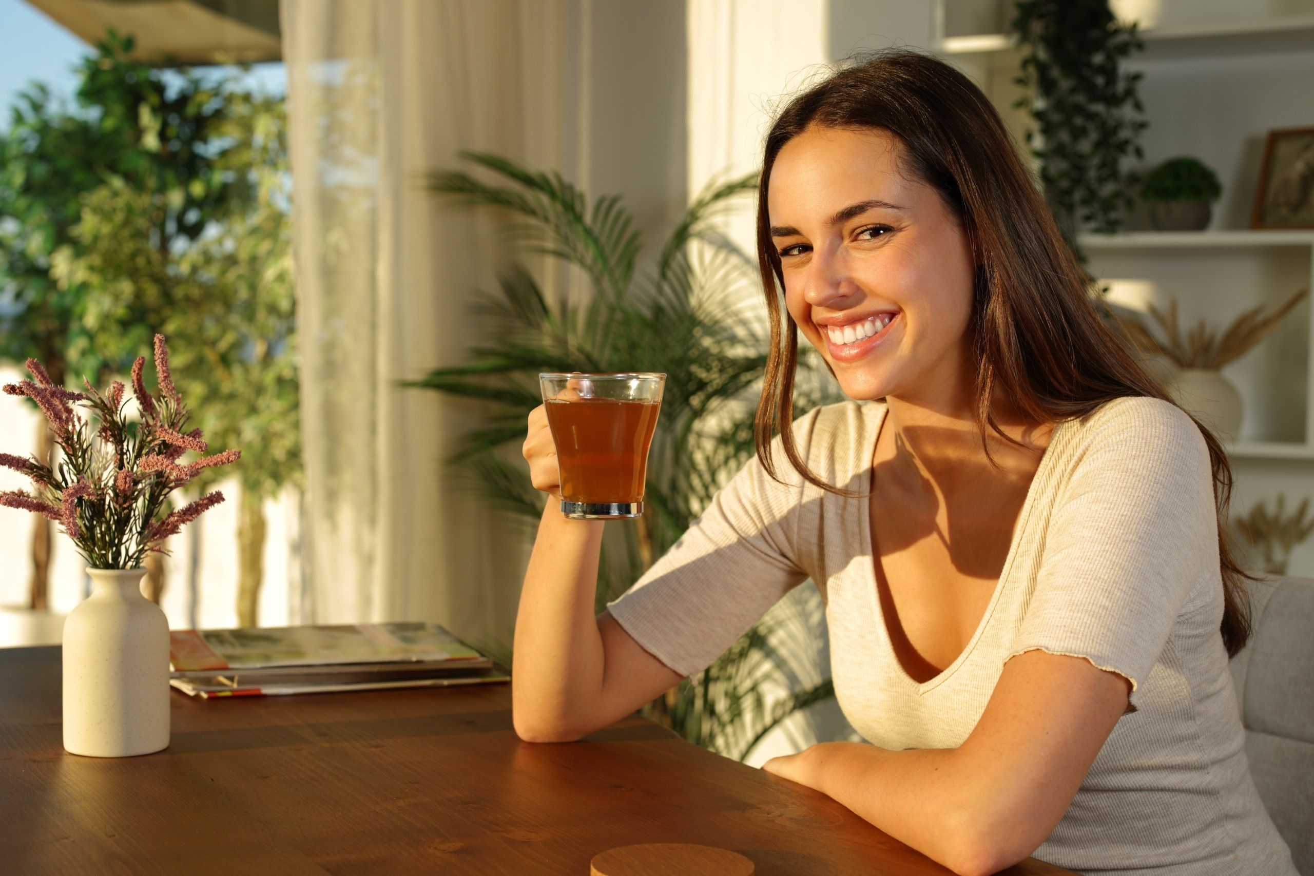 Happy,Woman,Drinking,Tea,Looks,At,Camera,Sitting,At,Home