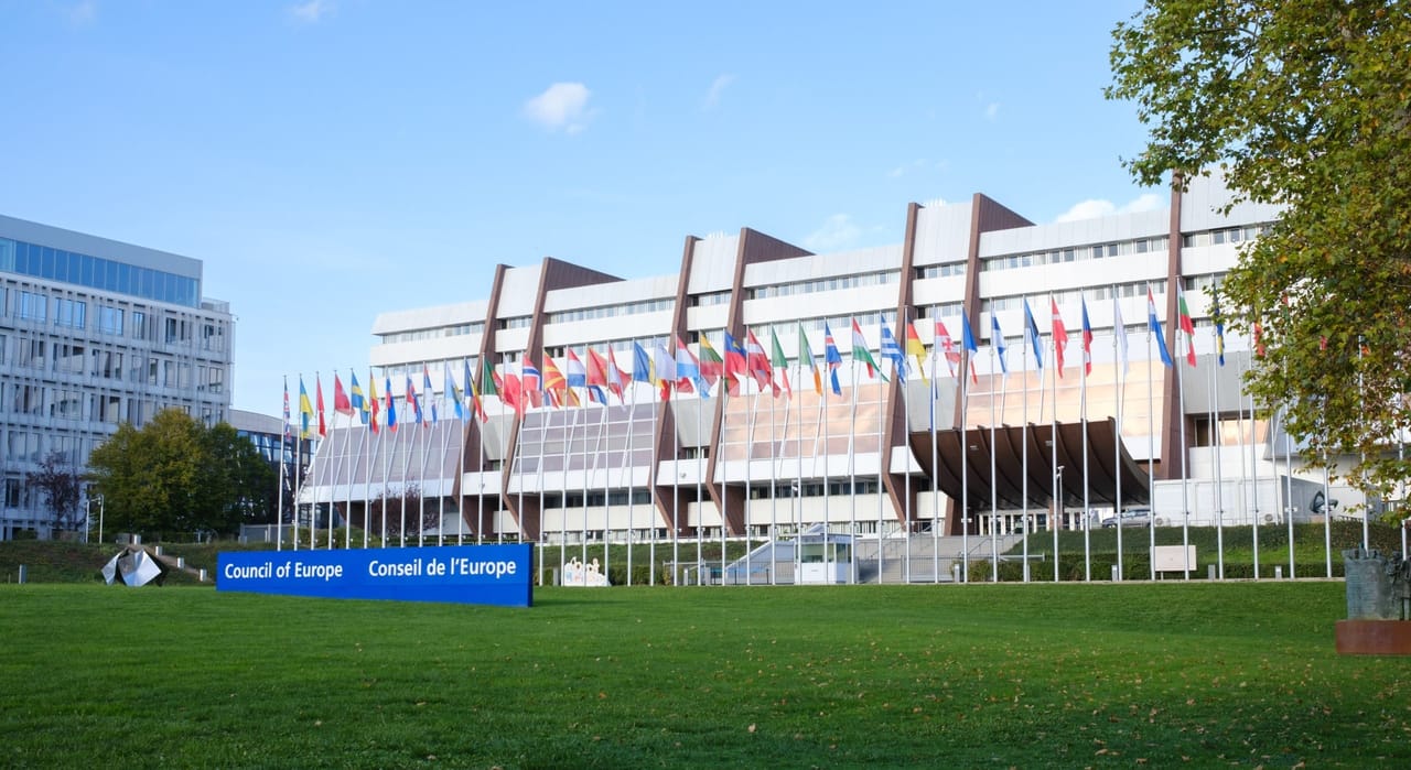 budynek siedziby Rady Europy w Strasburgu z szyldem „Council of Europe" i flagami państw członkowskich